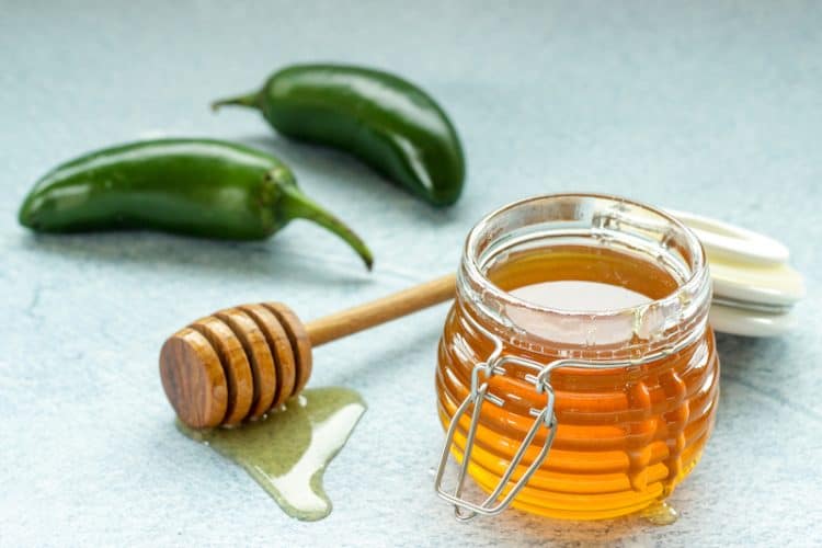 a small jar of honey with 2 jalapeno peppers