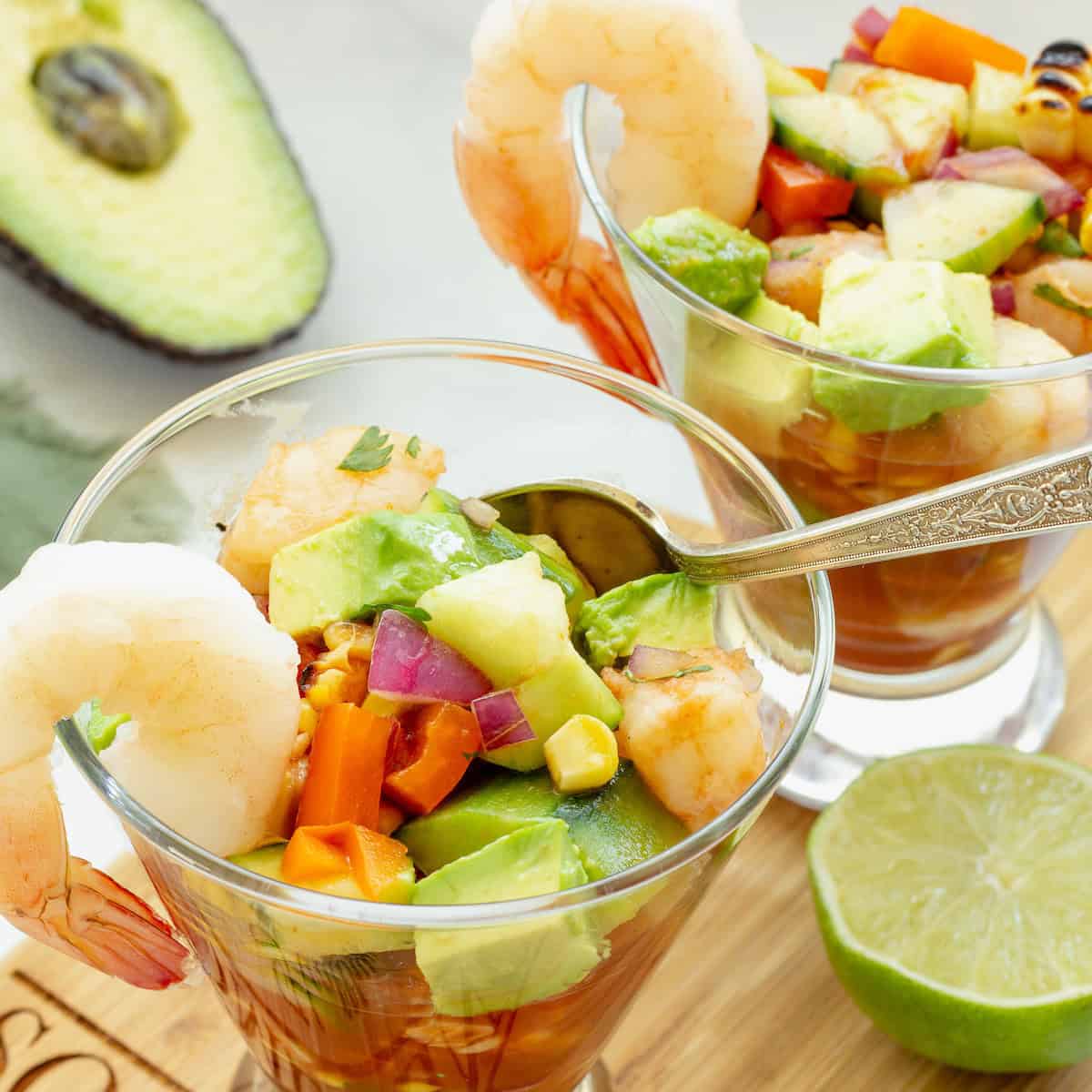 2 glasses with Mexican shrimp cocktail. A half of a lime and avocado are next to the glasses.