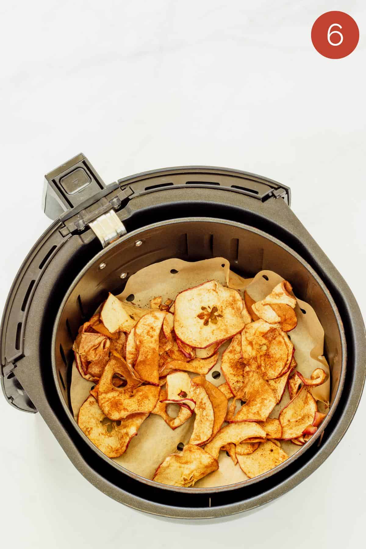 an air fryer basket with cooked air fryer apple chips