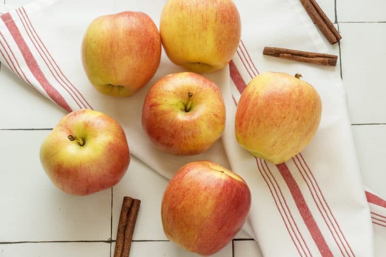 An overhead shot of gala apples and cinnamon sticks on a white and red dish towel