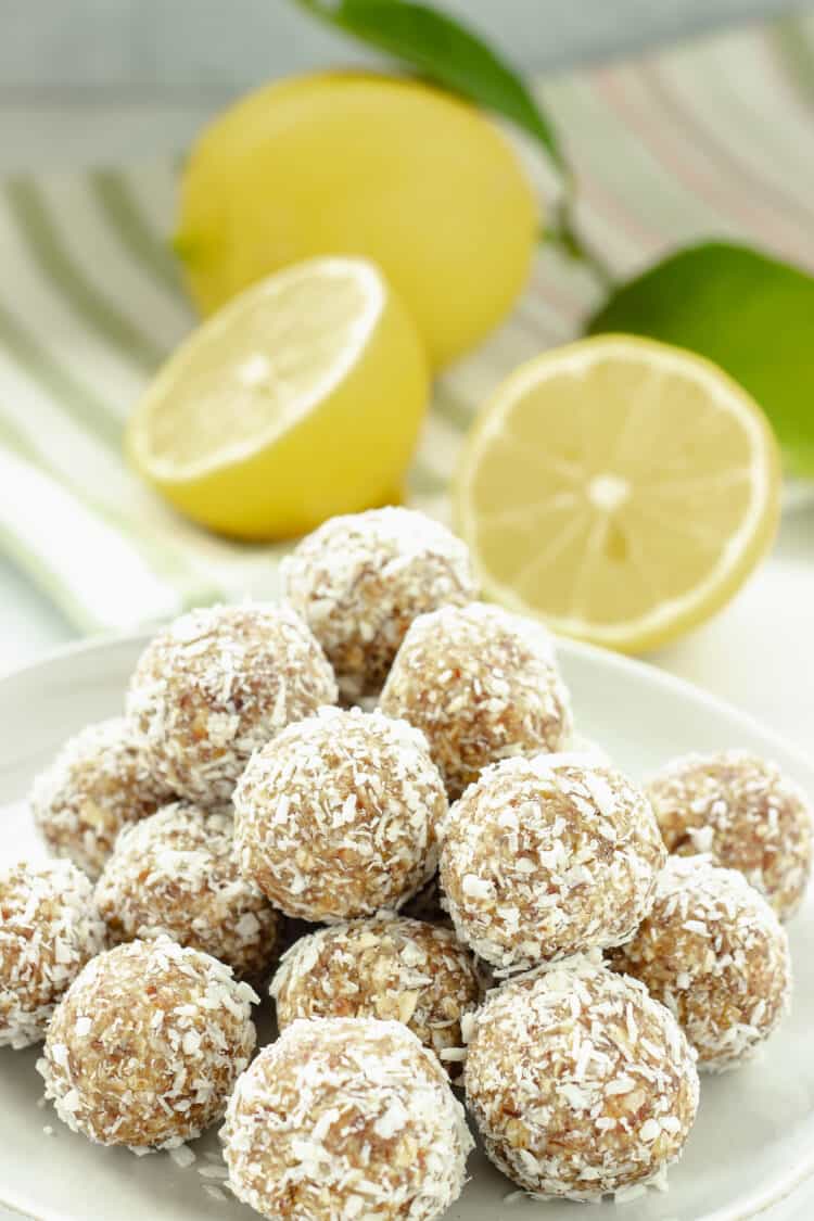 A plate of coconut covered energy bites with cut lemons in the background
