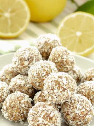 A plate of lemon coconut flaxseed balls with lemon halves in the background
