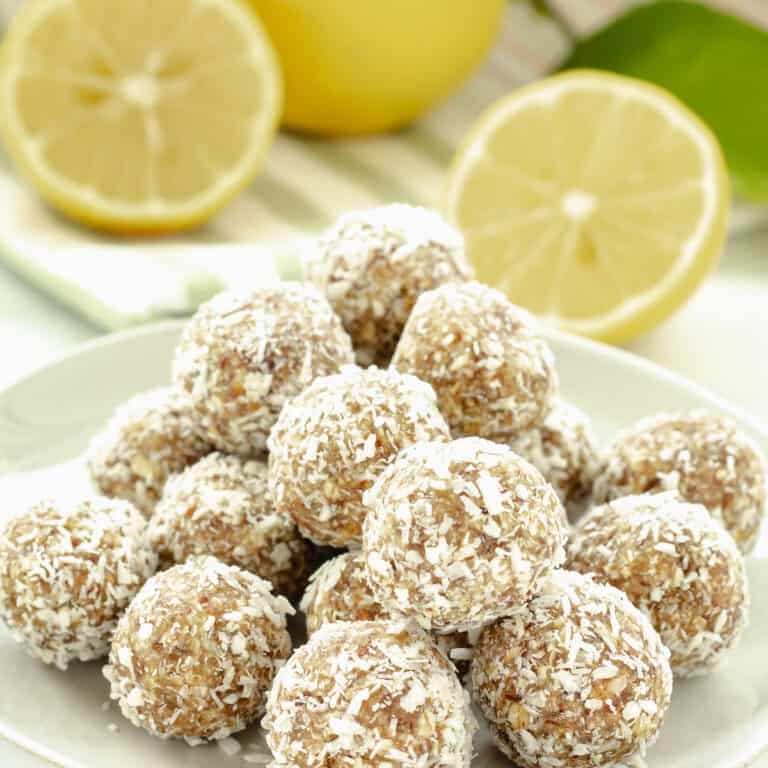A plate of lemon coconut flaxseed balls with lemon halves in the background