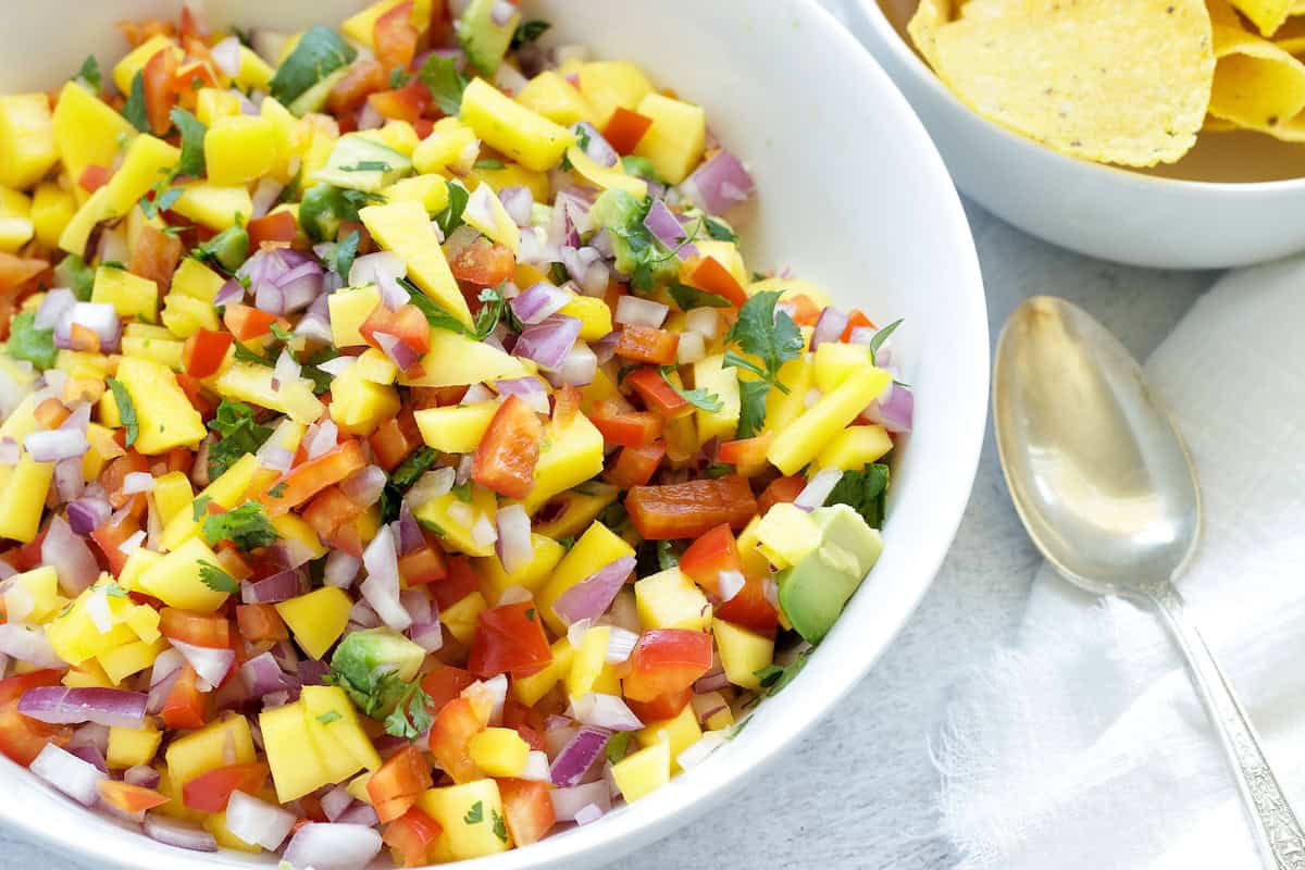 a white bowl of mango habanero salsa with a bowl of tortilla chips.