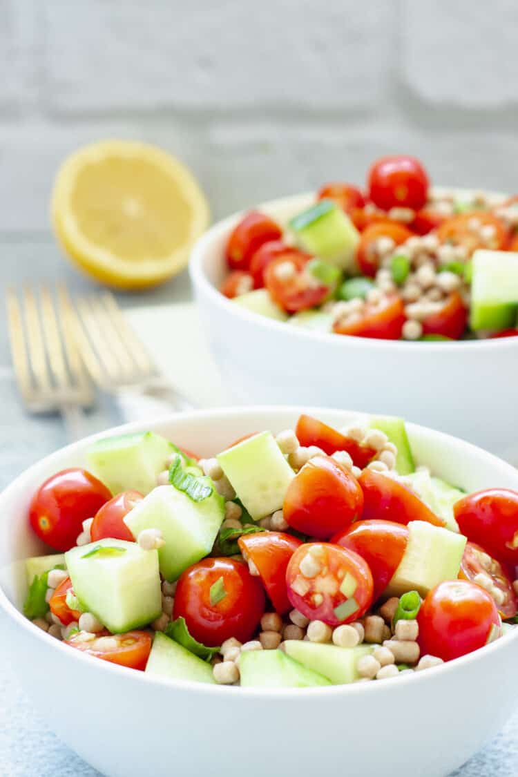 Two small white bowls of Mediterranean cucumber tomato salad with Israeli couscous.