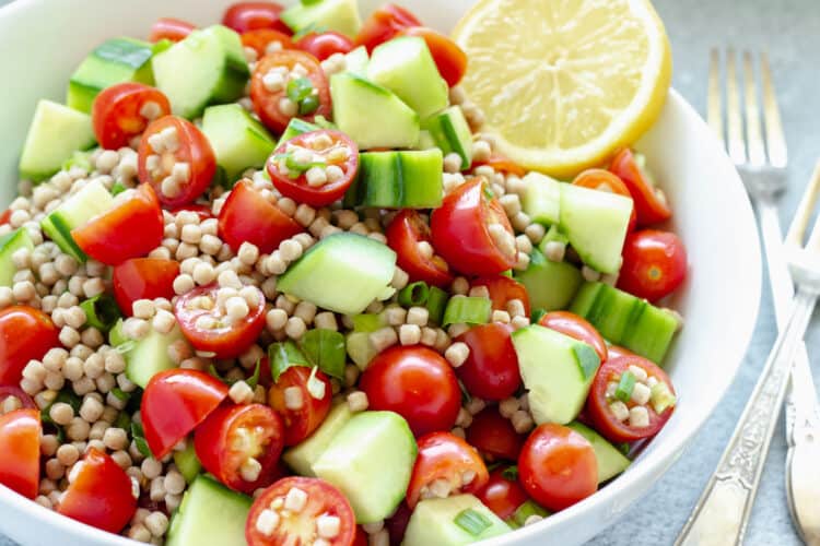 close up shot of Mediterranean cucumber tomato salad in a white bowl garnished with a lemon slice.