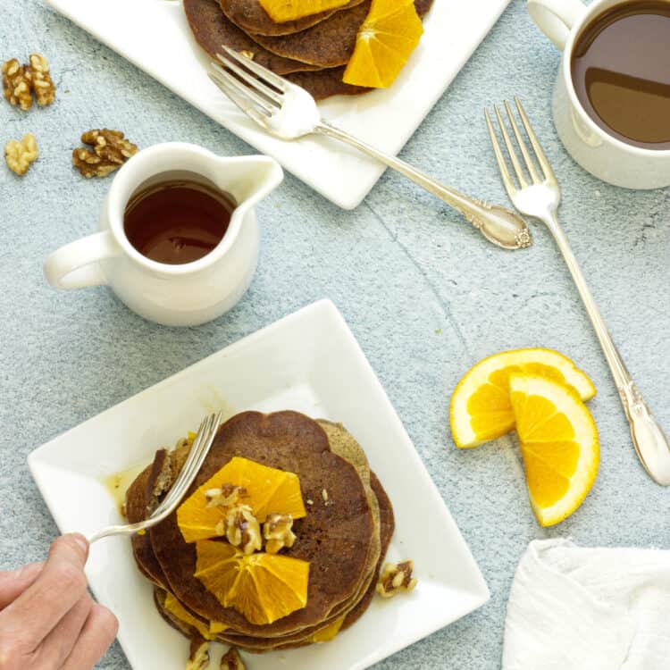 Overhead shot of 2 plates of buckwheat pancakes topped with orange segments.