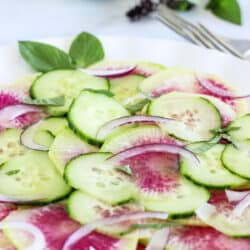 A white plate of Watermelon Radish Salad with thin sliced watermelon radishes, cucumbers, and red onions.