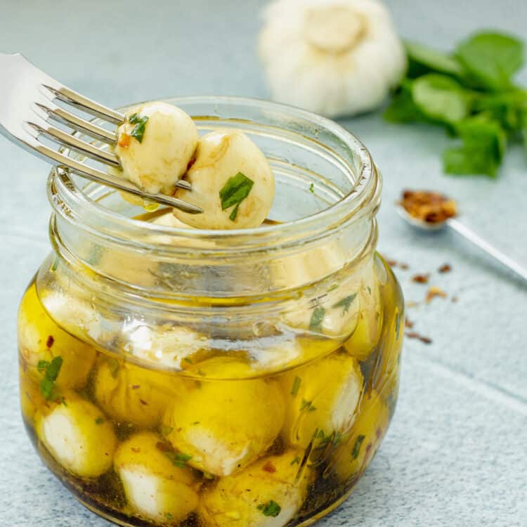 A closeup shot of a jar of mini ciliegine mozzarella balls marinated in olive oil, garlic, and herbs.