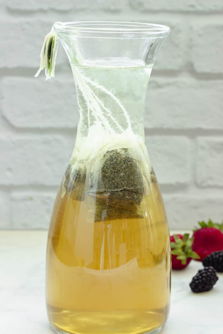 A carafe of green sun tea brewed for about two hours. Light green-brown in color.