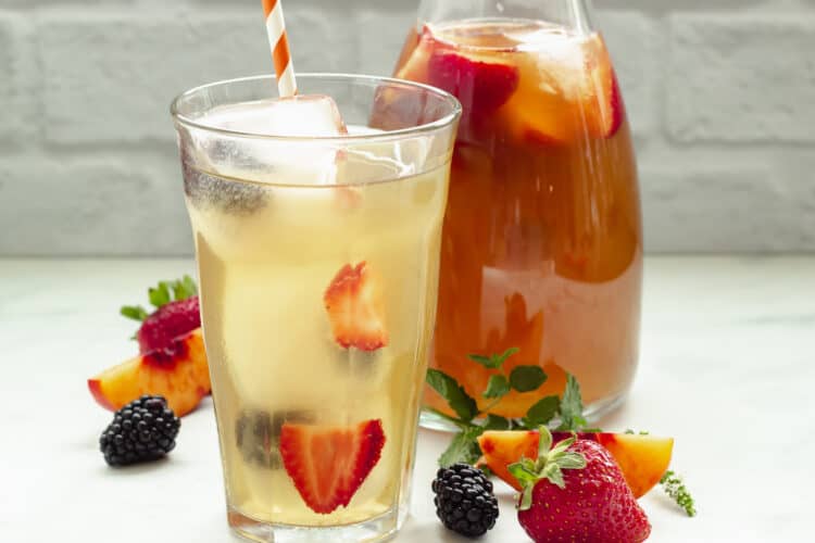 A glass of sun tea with fruit and a carafe of tea in the background