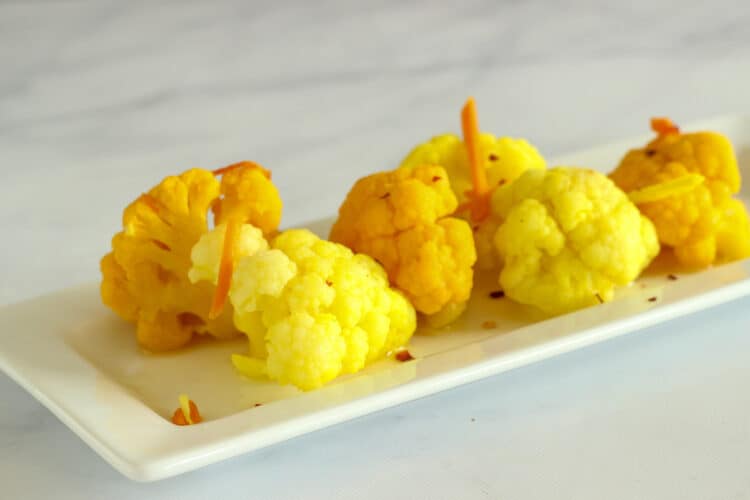 A closeup shot of turmeric and ginger pickled cauliflower florets on a white rectangular plate.
