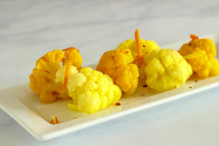 Pickled cauliflower florets on a white rectangular plate.