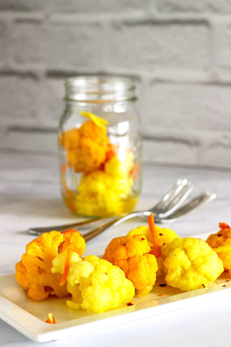 A closeup shot of a plate of pickled cauliflower with turmeric & ginger. A jar of pickled cauliflower is in the background.