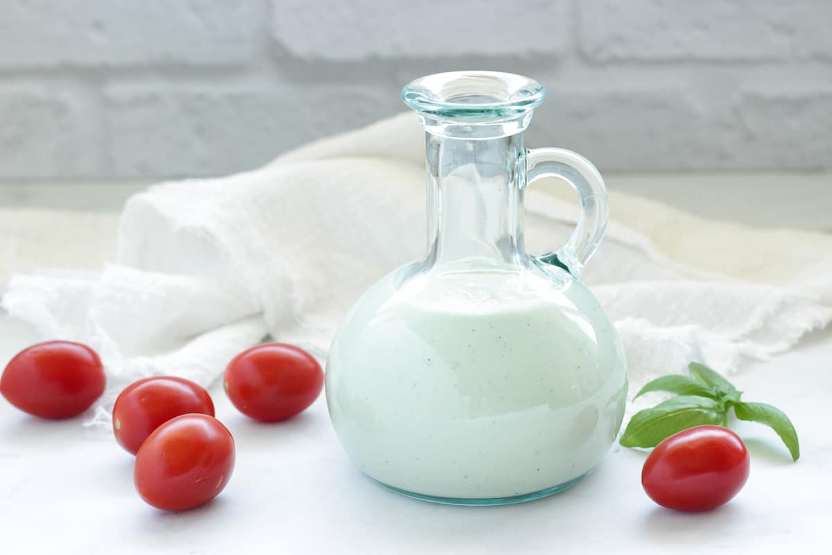  a bottle of homemade blue cheese vinaigrette salad dressing surrounded by cherry tomatoes and a sprig of basil