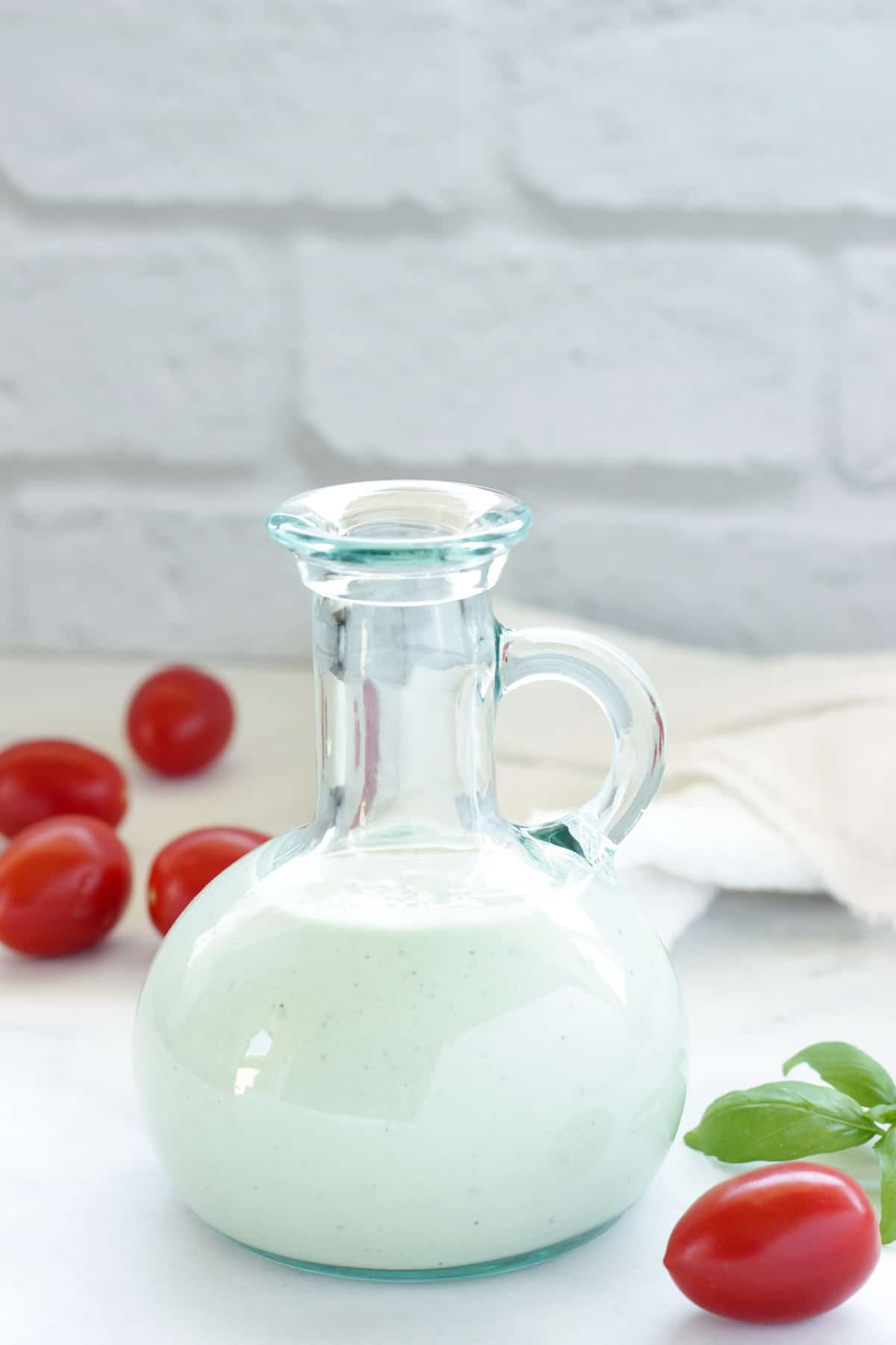 closeup of a bottle of homemade blue cheese vinaigrette salad dressing surrounded by cherry tomatoes and a sprig of basil