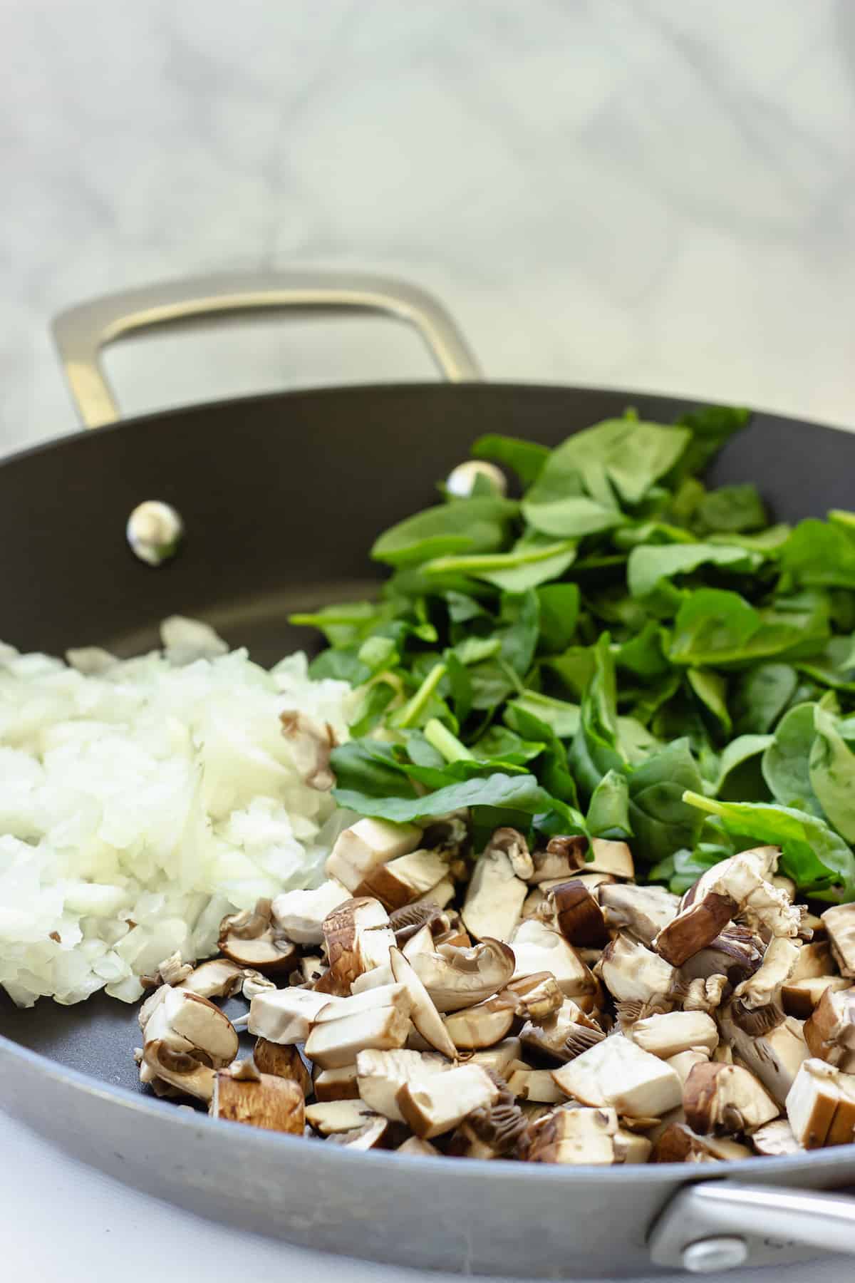 a saute pan with chopped mushrooms, onions, and spinach