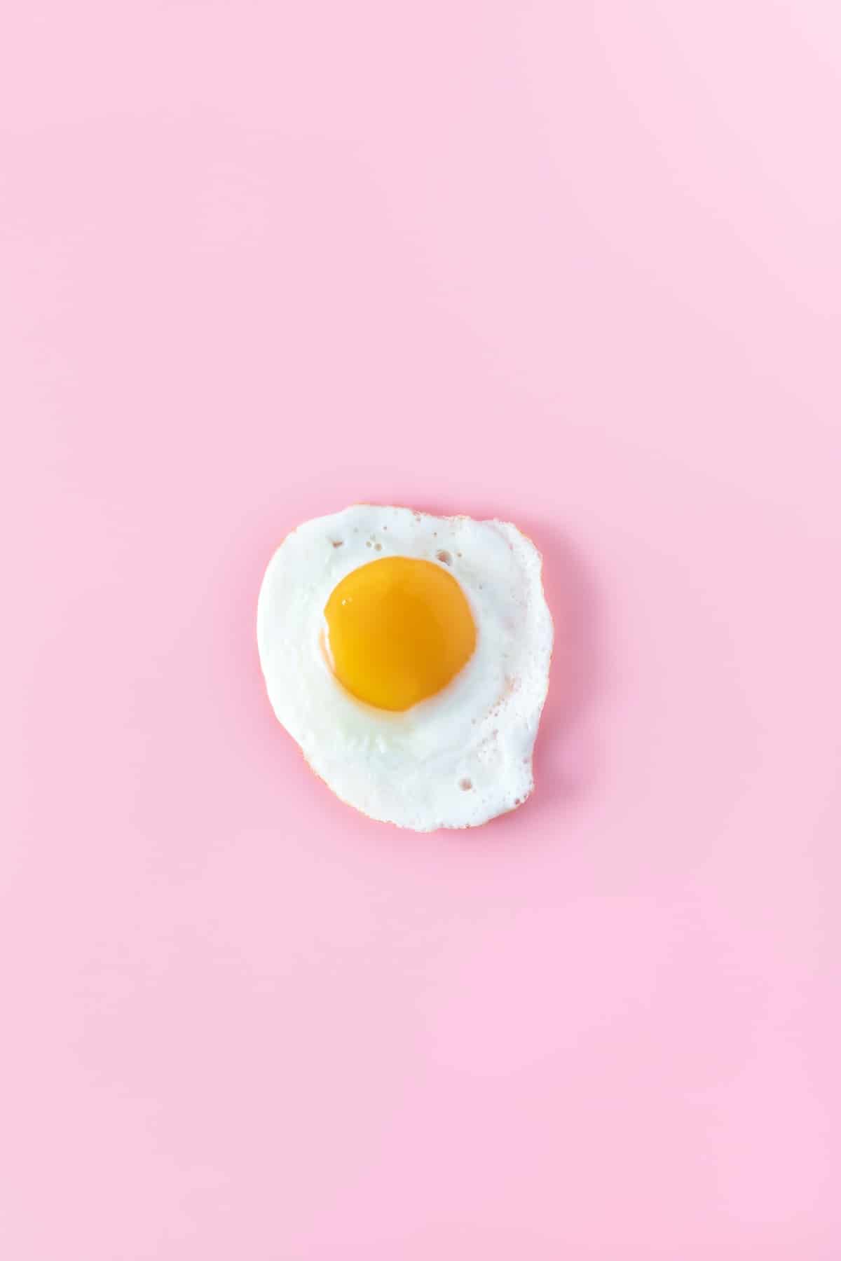 An overhead shot of a fried egg on a pink background.