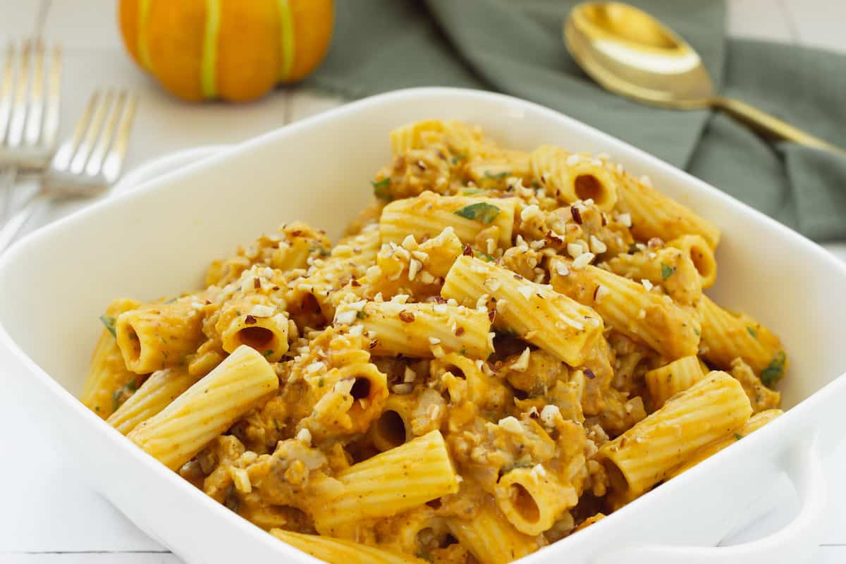 A white casserole dish filled with rigatoni and creamy pumpkin pasta sauce