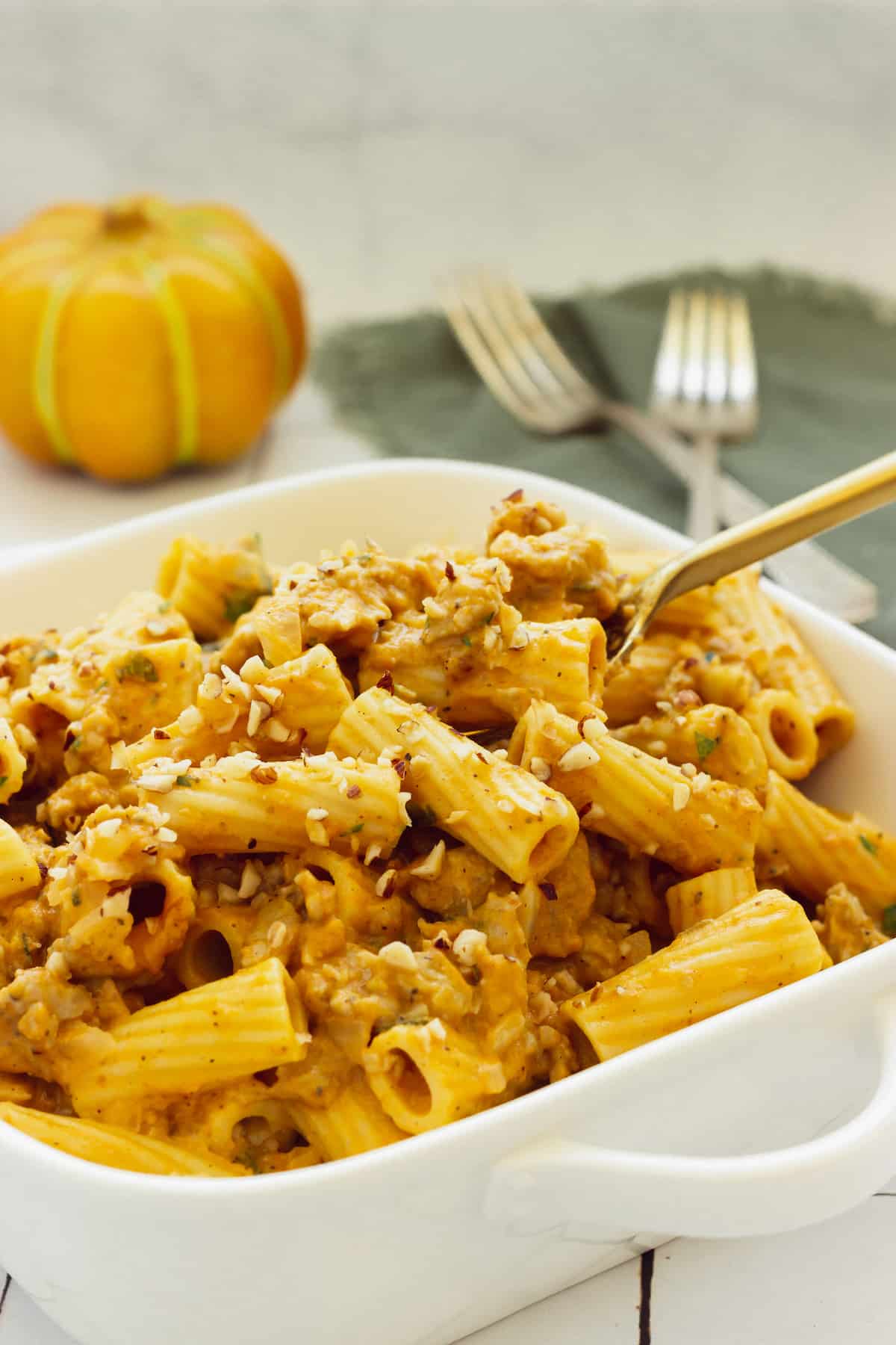 A white casserole dish filled with rigatoni with pumpkin pasta sauce.  