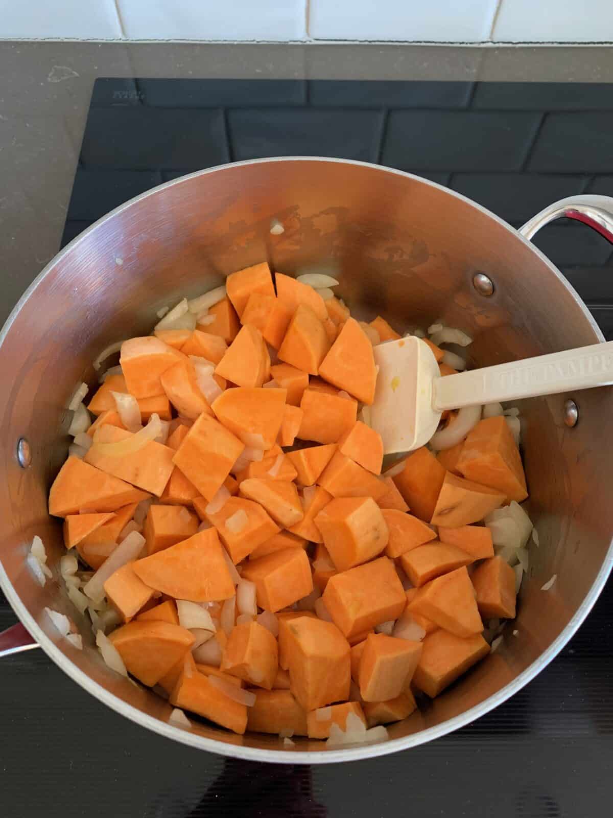 An overhead shot of a stockpot with cubed sweet potatoes and chopped onions.