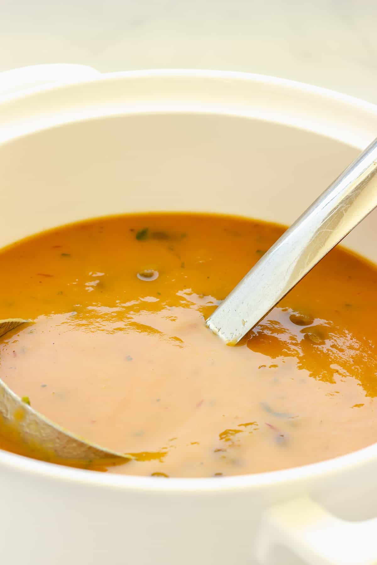 A white pot of orange-colored sweet potato black bean soup with a ladle in the soup.