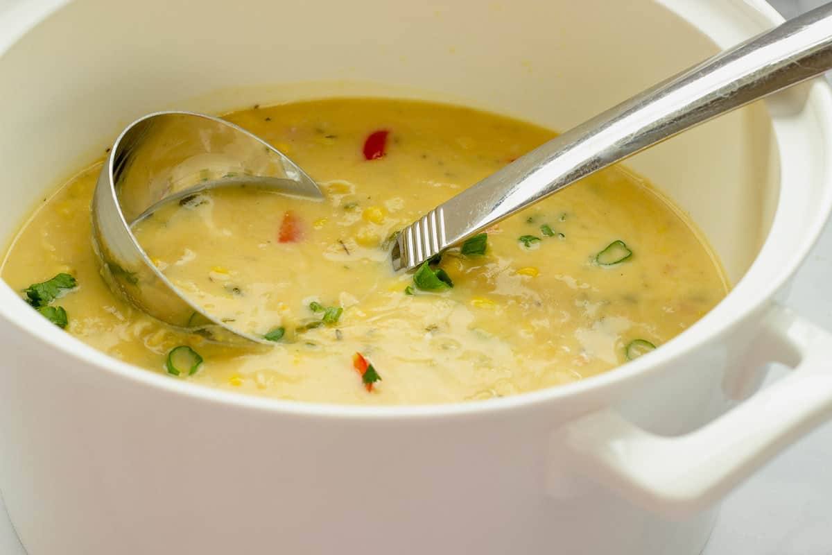 A white soup tureen and ladle with chicken corn chowder in the pot.