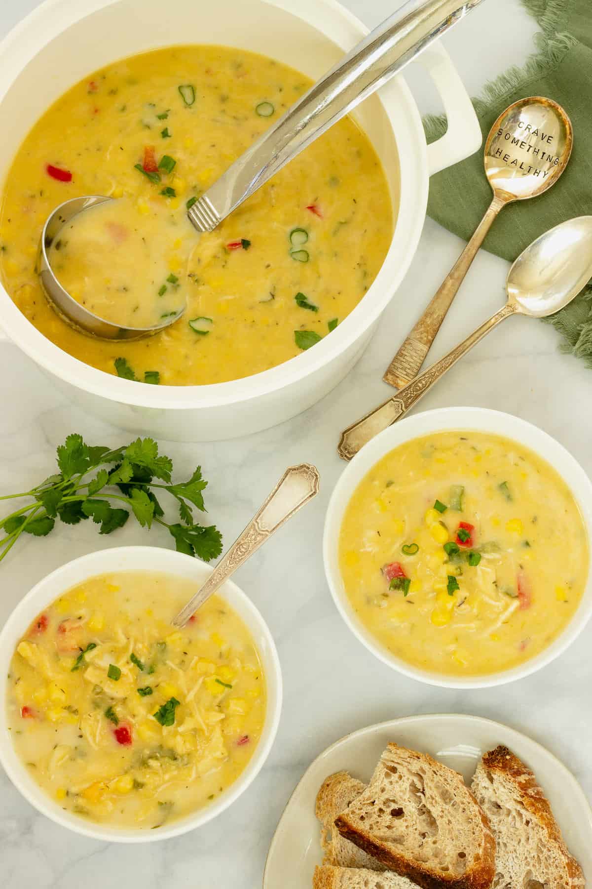 Overhead shot of a white soup pot with chicken and corn chowder and two bowls of the soup with spoons and a small plate of bread.