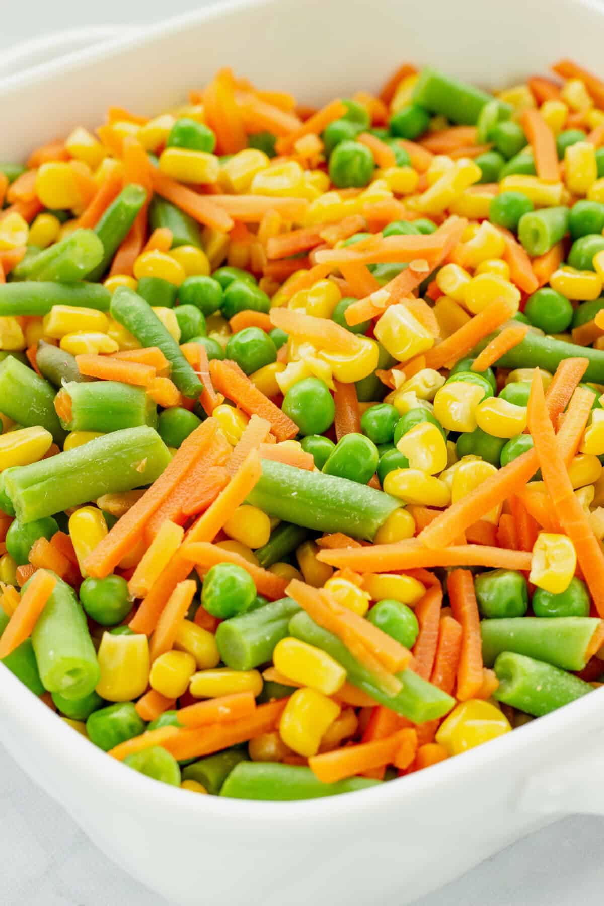 Step one of how to make mixed vegetable casserole. A white casserole dish with cooked mixed vegetables.