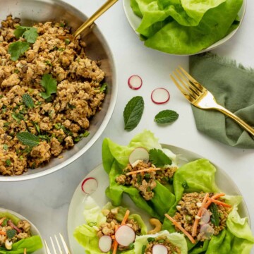 A white plate with tofu lettuce wraps. A skillet of the ground tofu filling and a bowl of lettuce leaves are in the background.