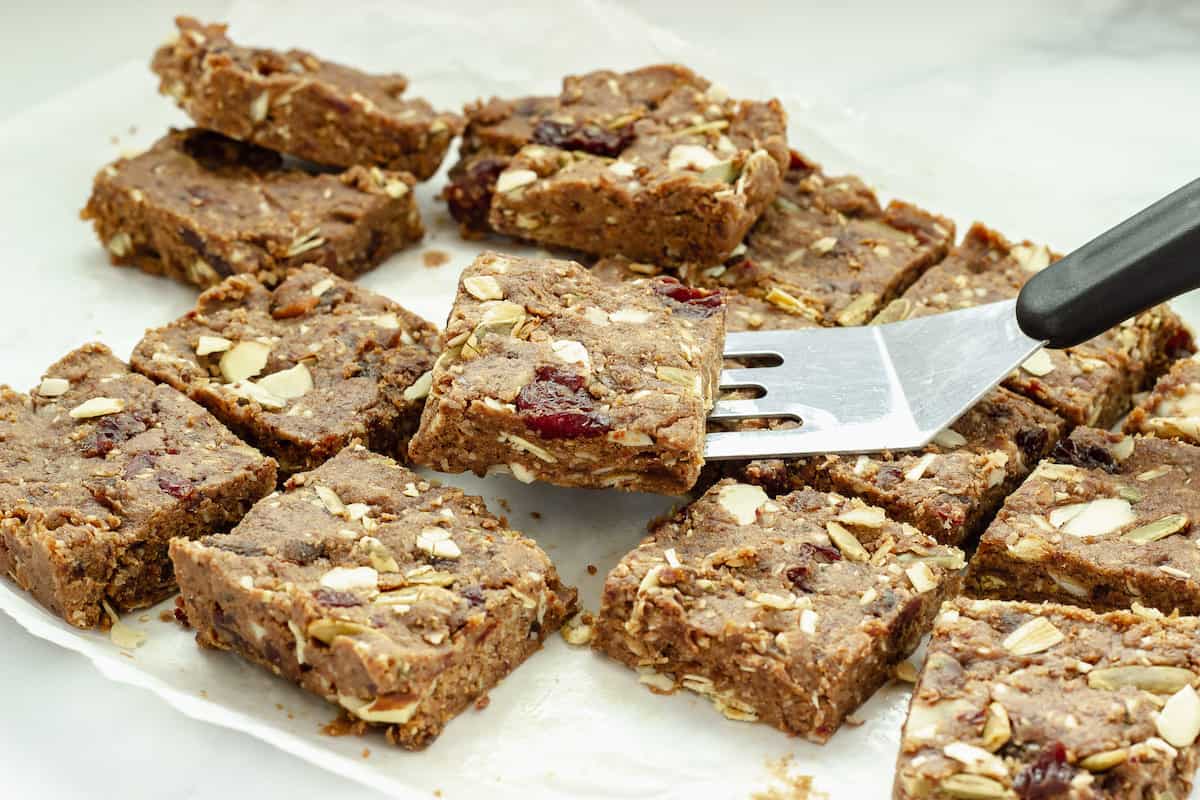 Fruit and nut bars on a sheet of parchment paper. A spatula is lifting one bar away from the rest.