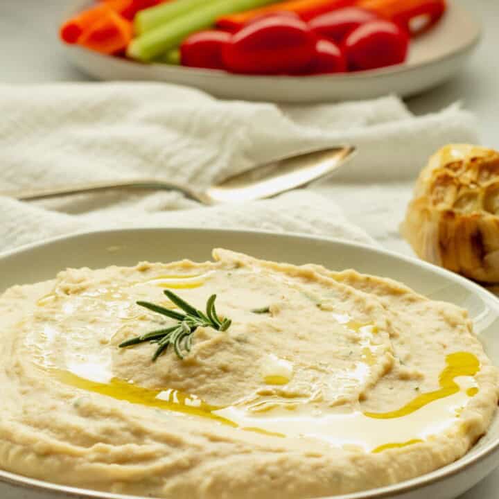 A plate spread with white bean dip. A white napkin and and cut vegetables are also on the table.