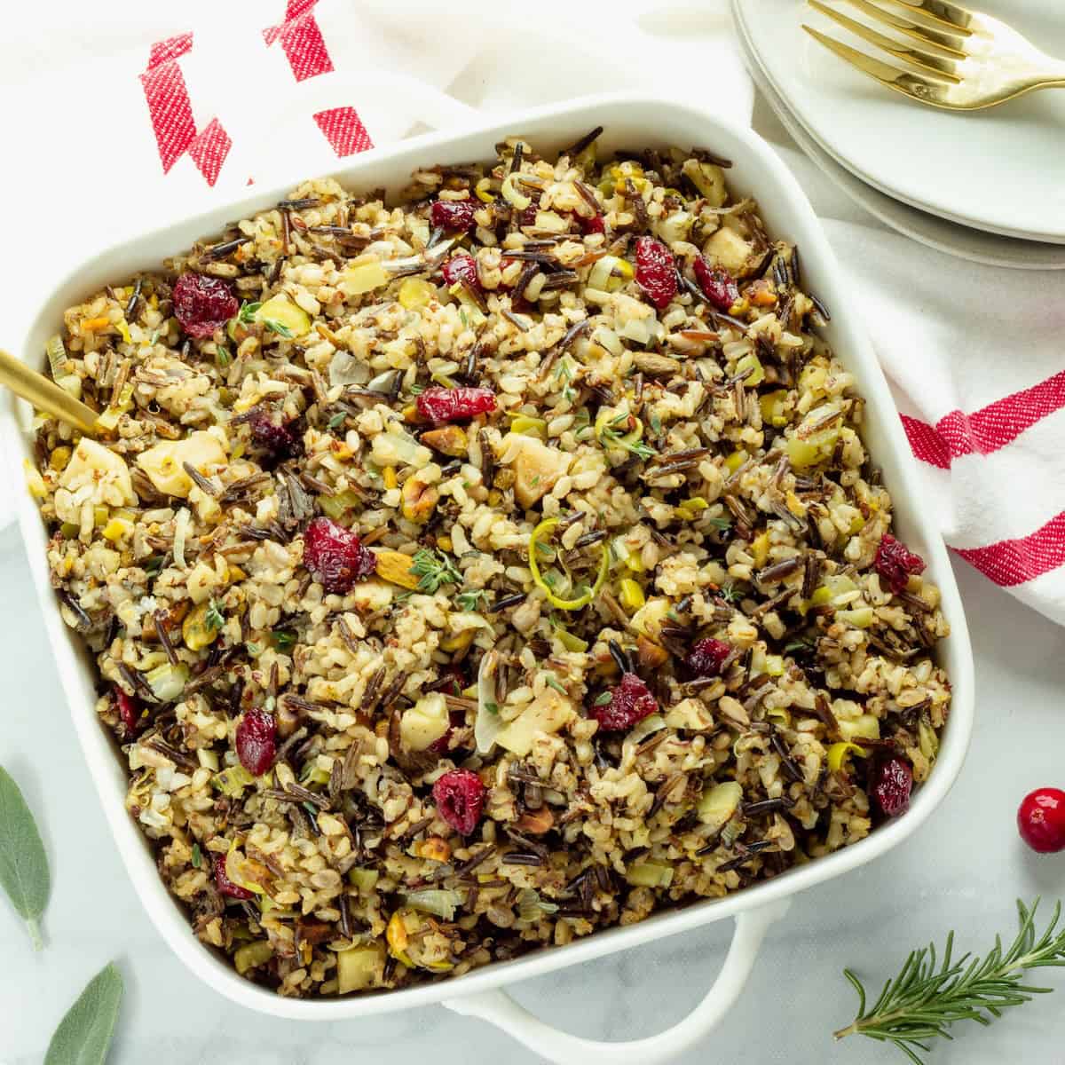 A square white casserole dish with wild rice stuffing on a white and red striped napkin.