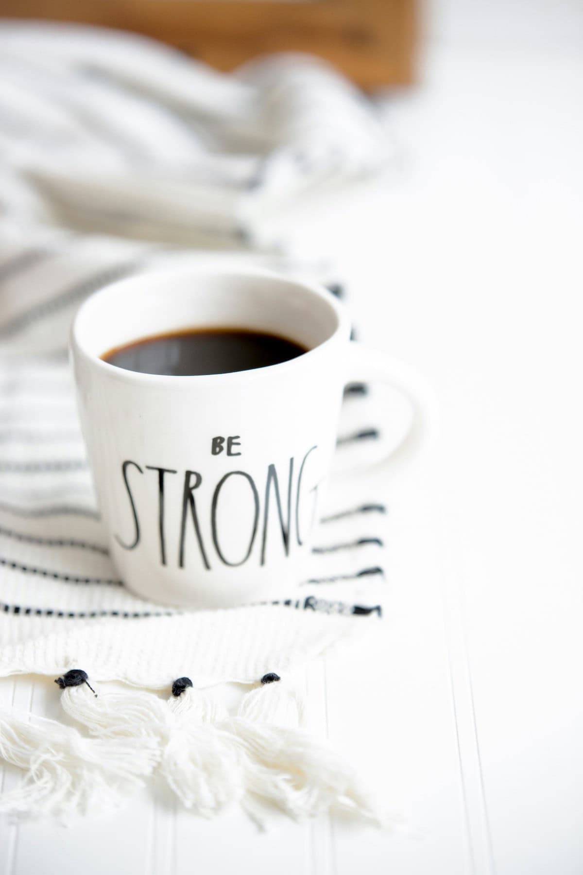 a cup of coffee on a white and black towel. The coffee cup says Be Strong.