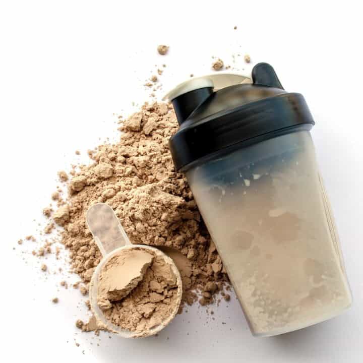 A scoop of chocolate protein powder with a mixer bottle.