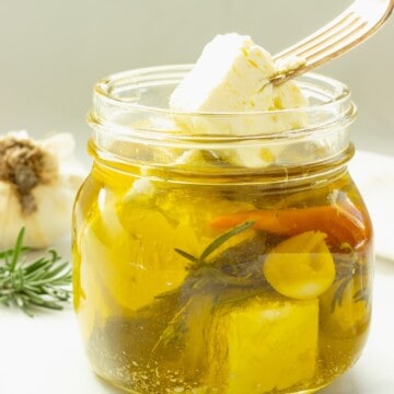 A jar of marinated feta cheese with a fork lifting a cube of feta from the jar.