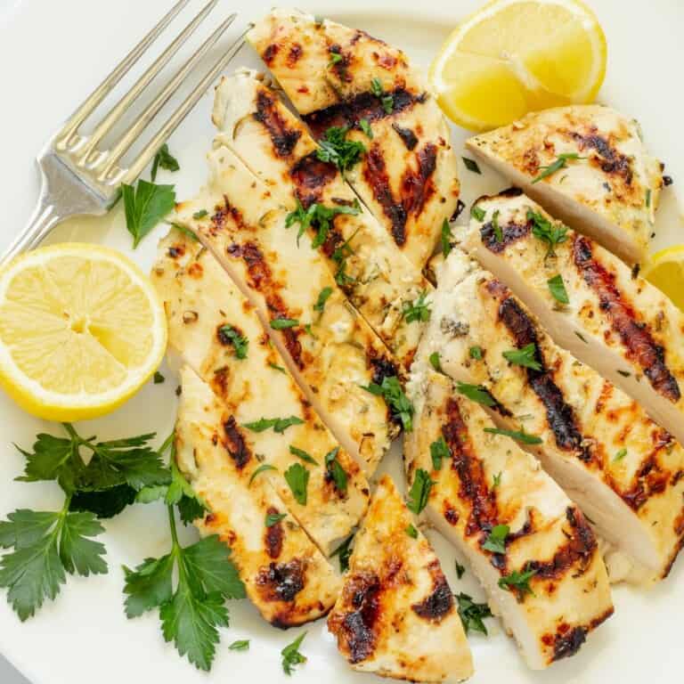 A platter of sliced Greek yogurt marinated chicken with lemon slices and parsley.
