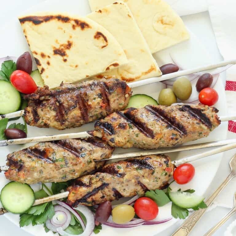 A platter of chicken kofta garnished with cucumber tomato salad, olives, and pita bread.