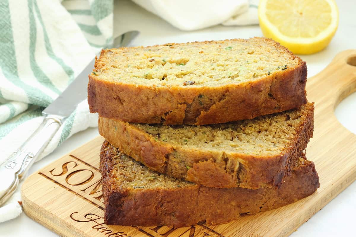 Three stacked slices of healthy lemon zucchini bread on a wood board.