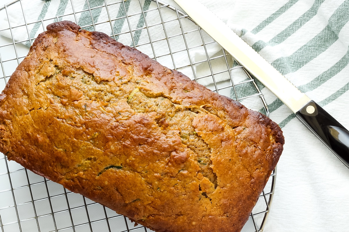 A loaf of healthy lemon zucchini bread in the pan on a cooling rack.